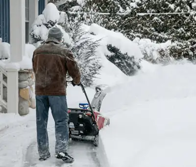 Residential snow removal technician using a snow blower to clear a home driveway and walkway in Aurora, CO